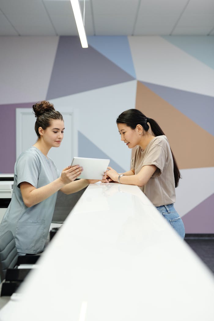 Two women interacting with a tablet at a modern reception desk indoors.